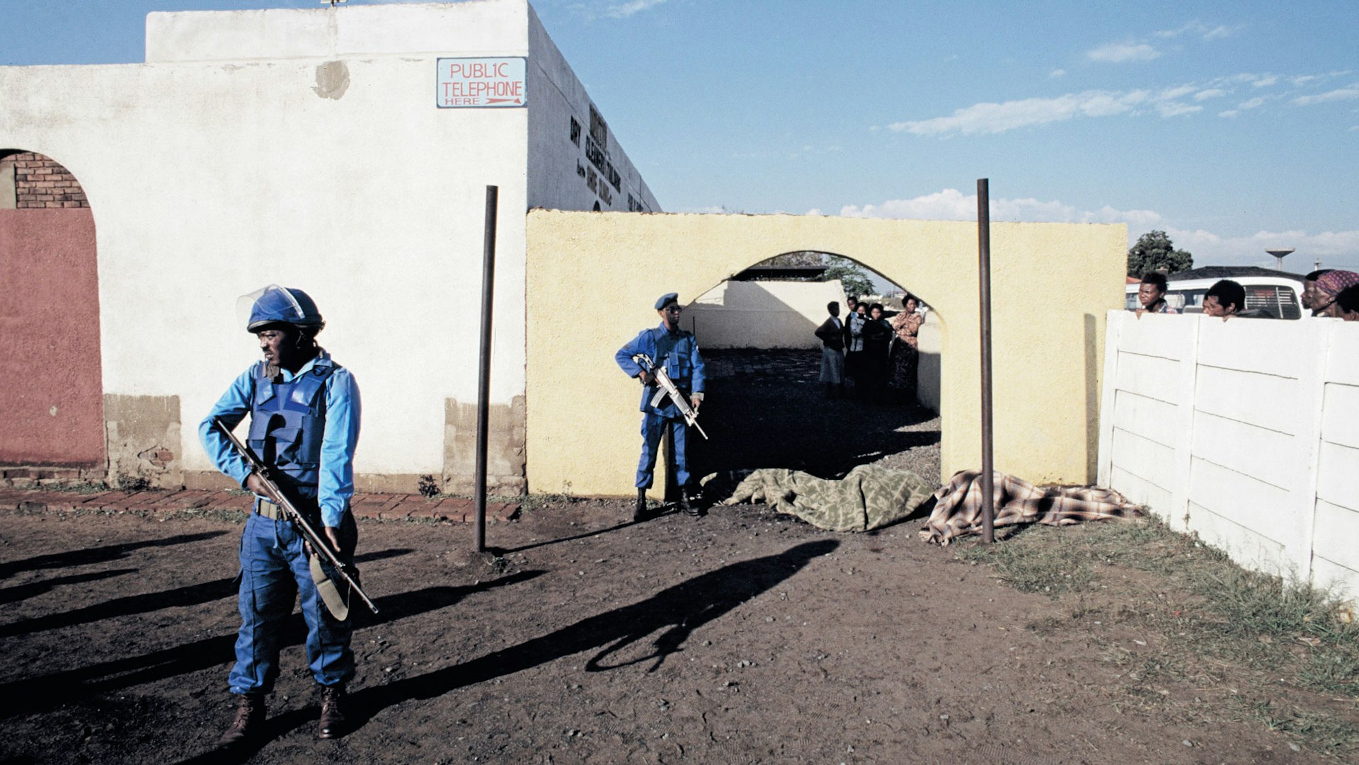 THEN: Members of the National Peacekeeping Force stand guard over the  bodies of three young men who were shot dead outside a tavern in Katlehong, 1994. 