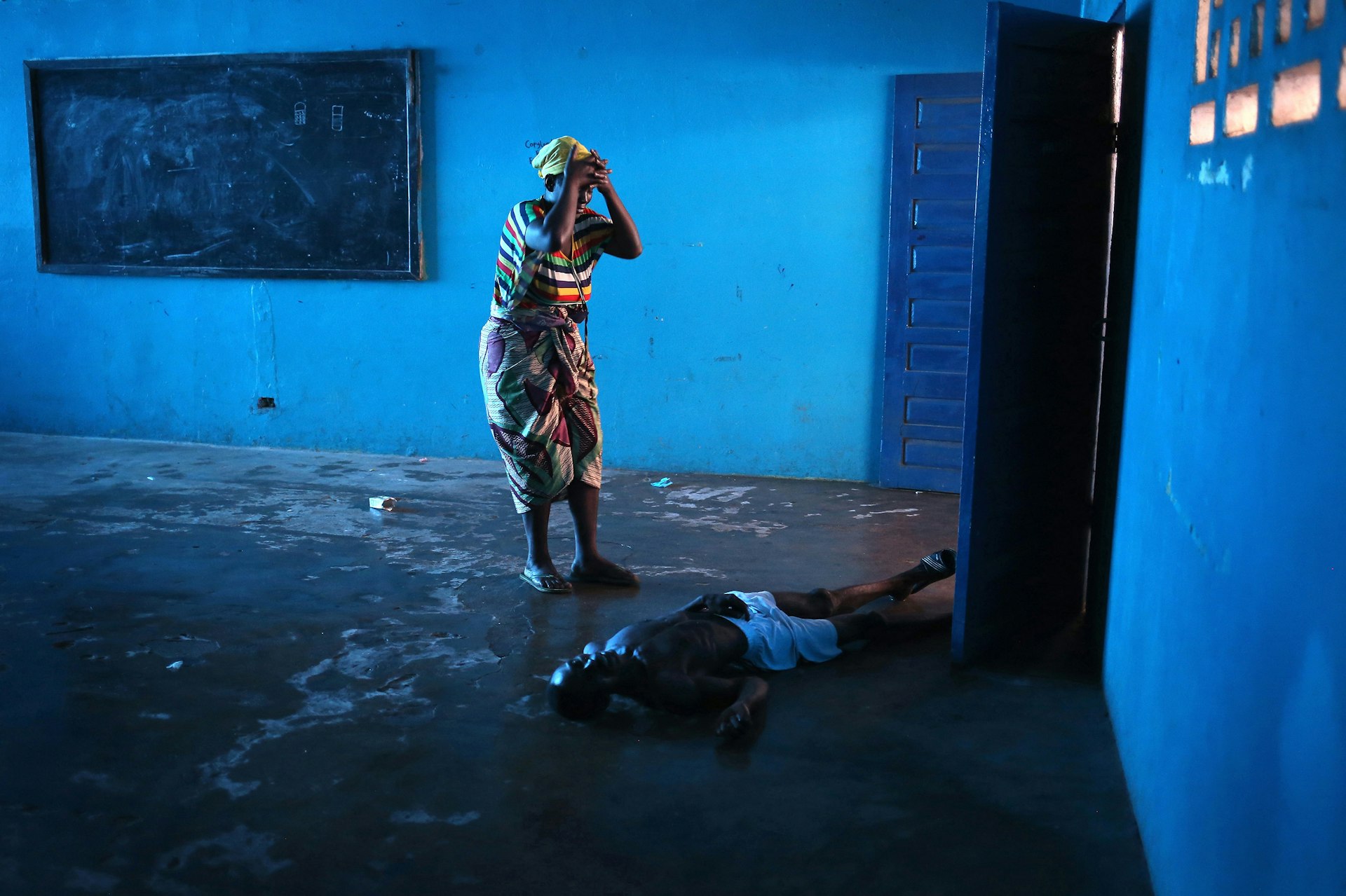 Omu Fahnbulleh stands over her husband Ibrahim after he fell and died in a classroom used for Ebola patients. John Moore / Getty Images, US, L'Iris d'Or, 2015 Sony World Photography Awards.
