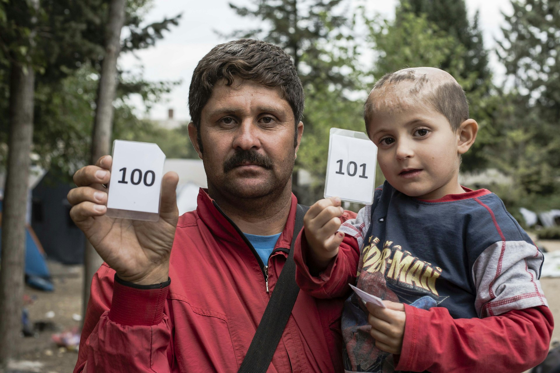 Abdul with his son who was injured in a barrell bomb attack in Syria. As part of registration in Serbia they are given a number in line. Their next step in Hungary.