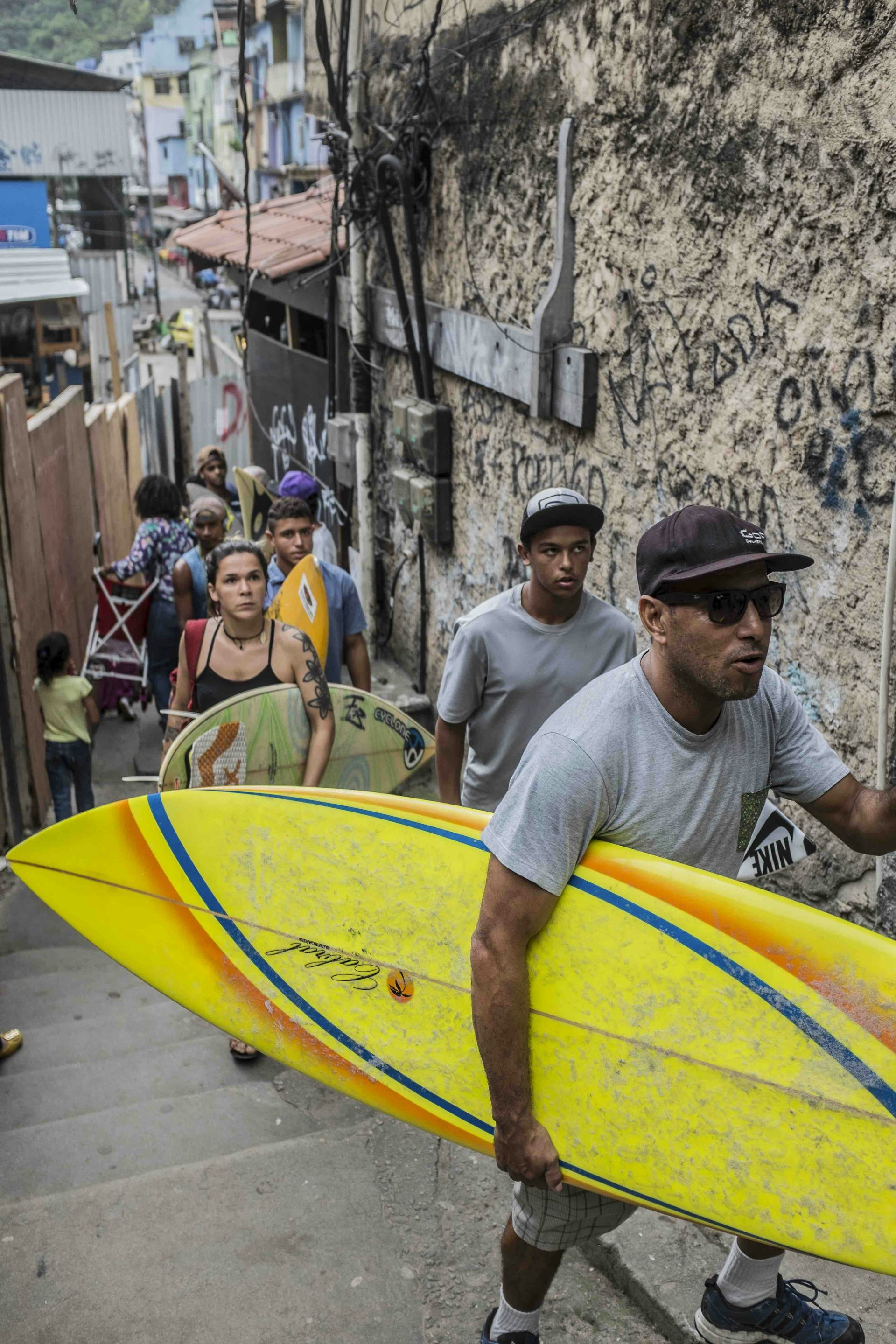 Young surfers, led by surf school founder Bocão, climb Rocinha's narrow streets.