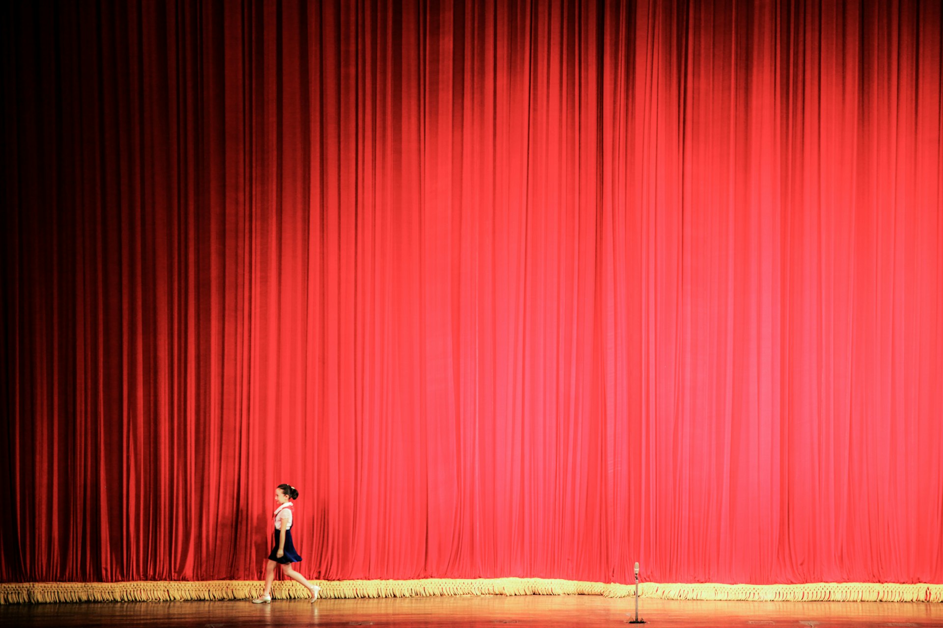 A young singer walking past the red curtain of a theatre inside the Children's Palace, Pyongyang.