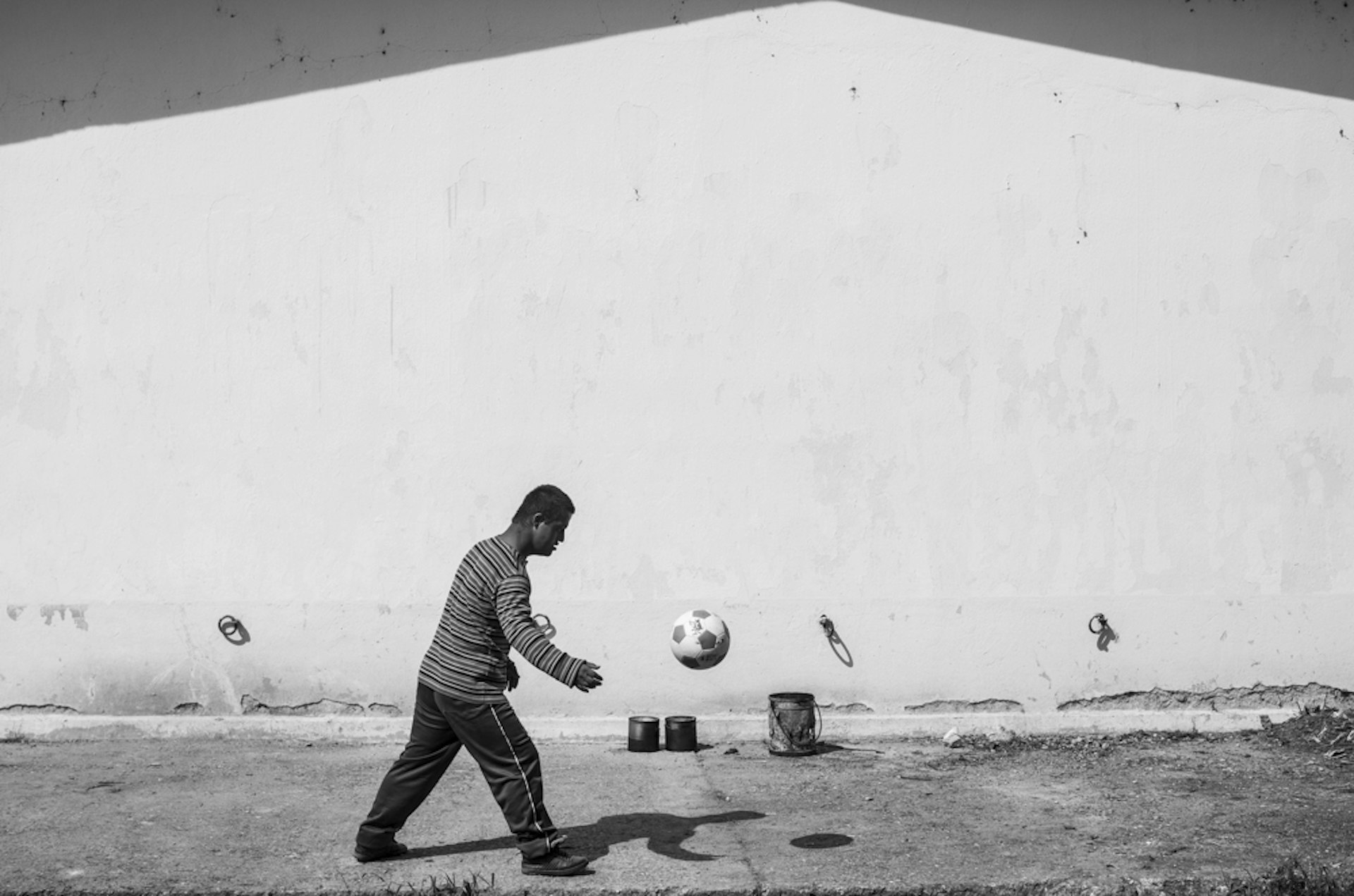A Yazidi boy plays football against a wall that houses refugee families.