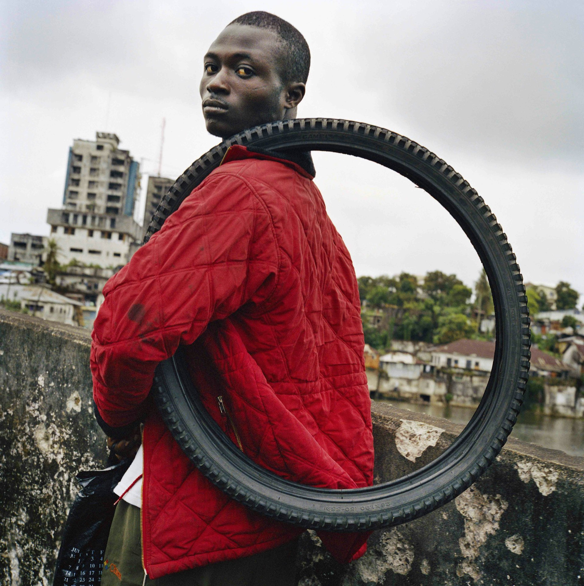 LIBERIA. 2003. Young man on the Gabriel Tucker bridge in central Monrovia carries a tyre which he is trying to sell. Liberia is one of the world's largest rubber producers and home to the Firestone Rubber Plantation. © Tim Hetherington / Magnum Photos