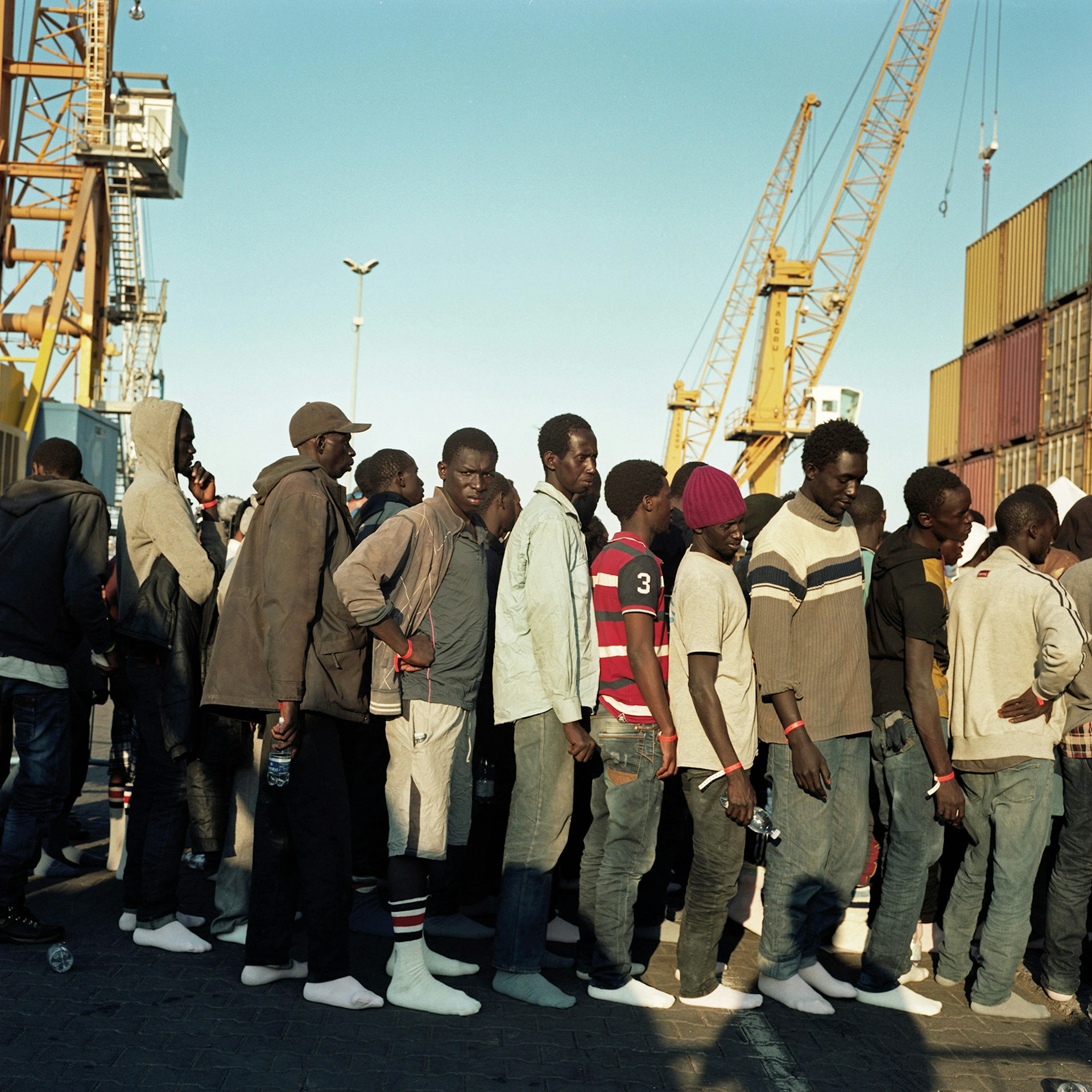 Port of Catania, Sicily, Italy, June 2015. A queue of migrants wait to be processed by the Italian authorities. Upon arrival the first items people are given by the Italian Red Cross, are a bottle of water and a pair of white socks.