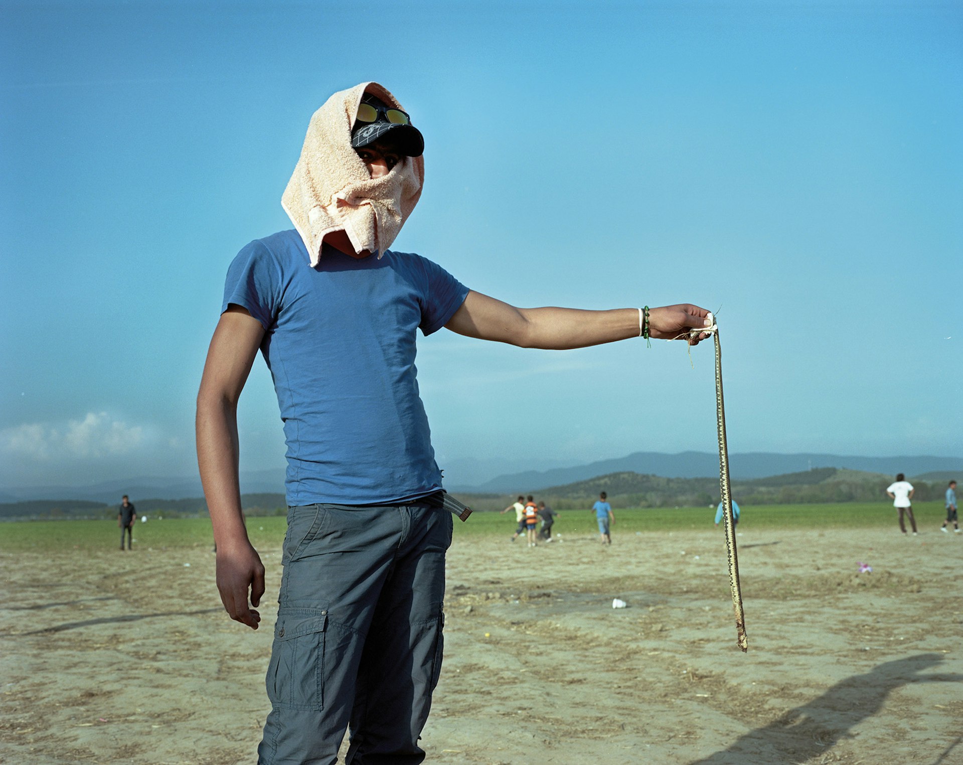 Idomeni, Greece, April 2016. Man holds a snake that he found and killed near a children’s play area.