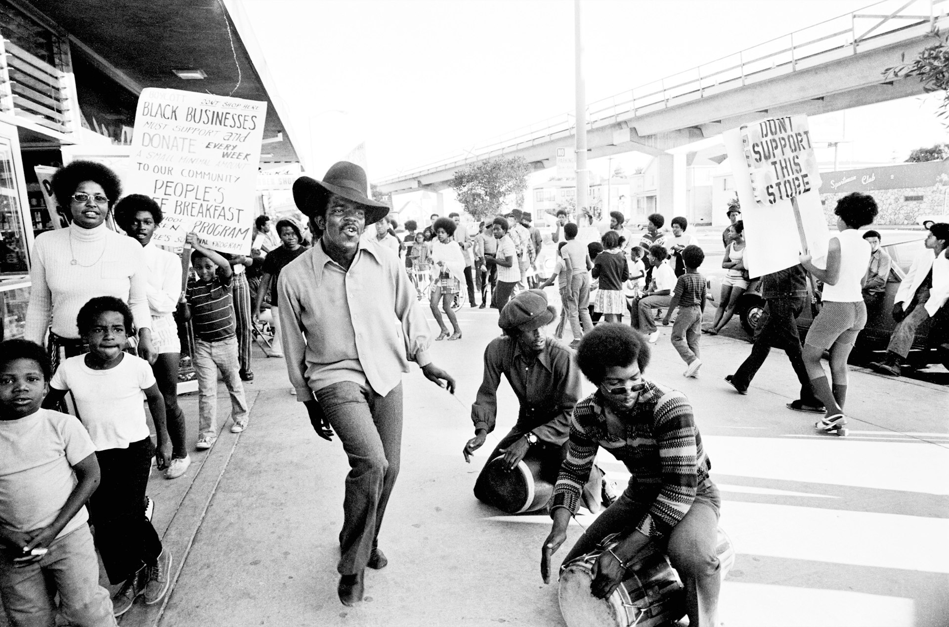 The Lumpen, the Panthers’ singing group, performs at the boycott of Bill’s Liquors, Oakland, 1971. Clark Bailey, known as Santa Rita, is dancing. Michael Torrence (front) and James Mott (back) are drumming.
