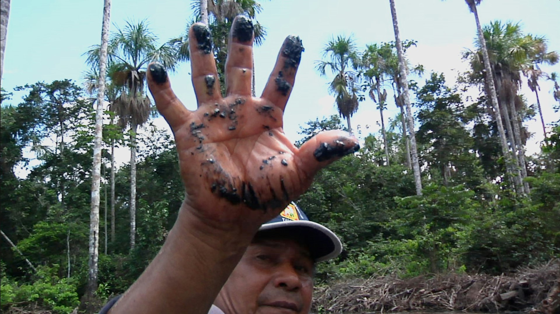 A local resident shows the oil residue left behind along an Amazon tributary from a pipeline spill that has supposedly been remediated. 