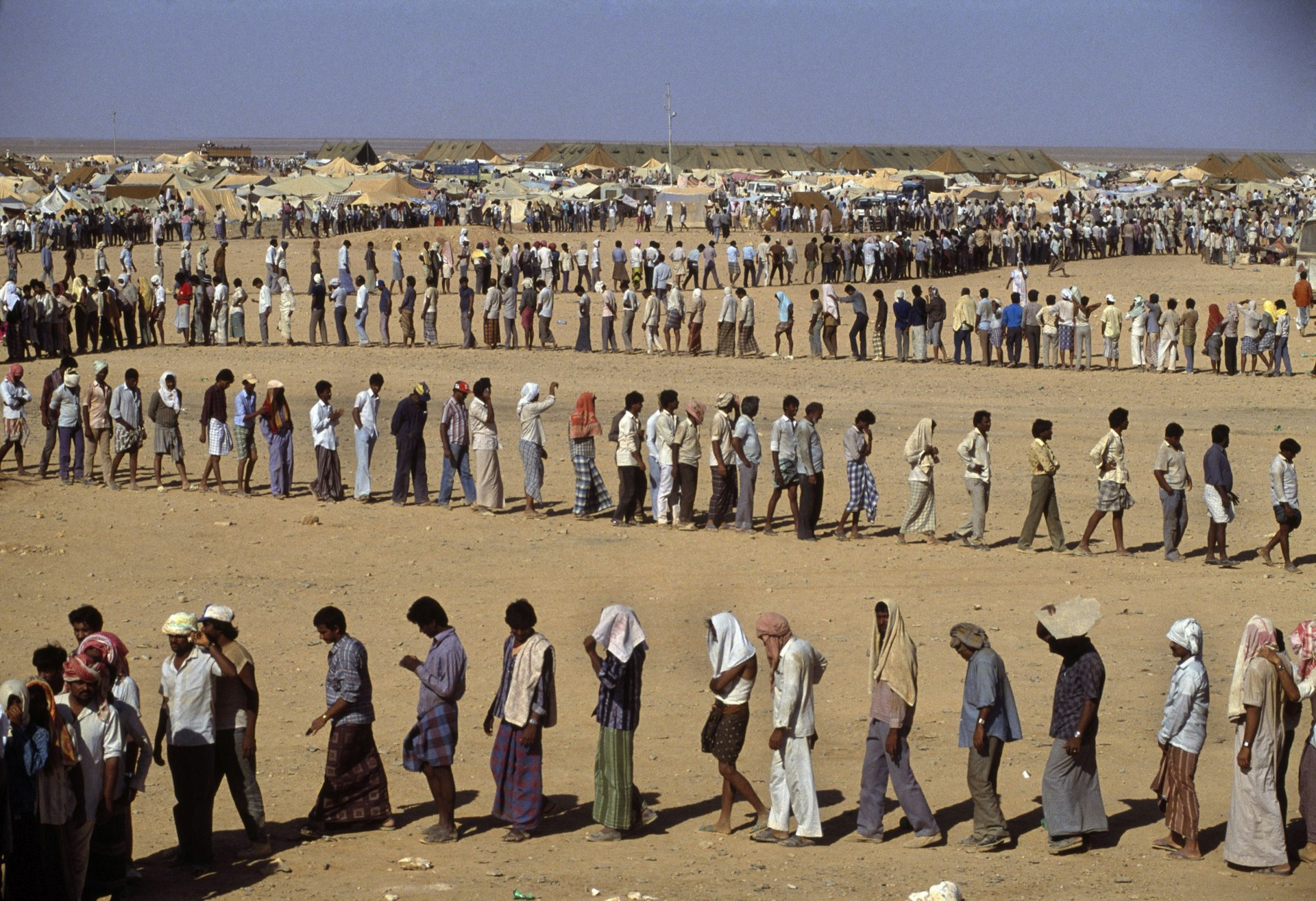 Refugees In the desert. The Sha-alaan One camp, is the worst camp. They have orderly food lines with thousands of refugees waiting calmly for food distribution from the CHARITAS charity organization. Jordan,1990 © Chris Steele-Perkins