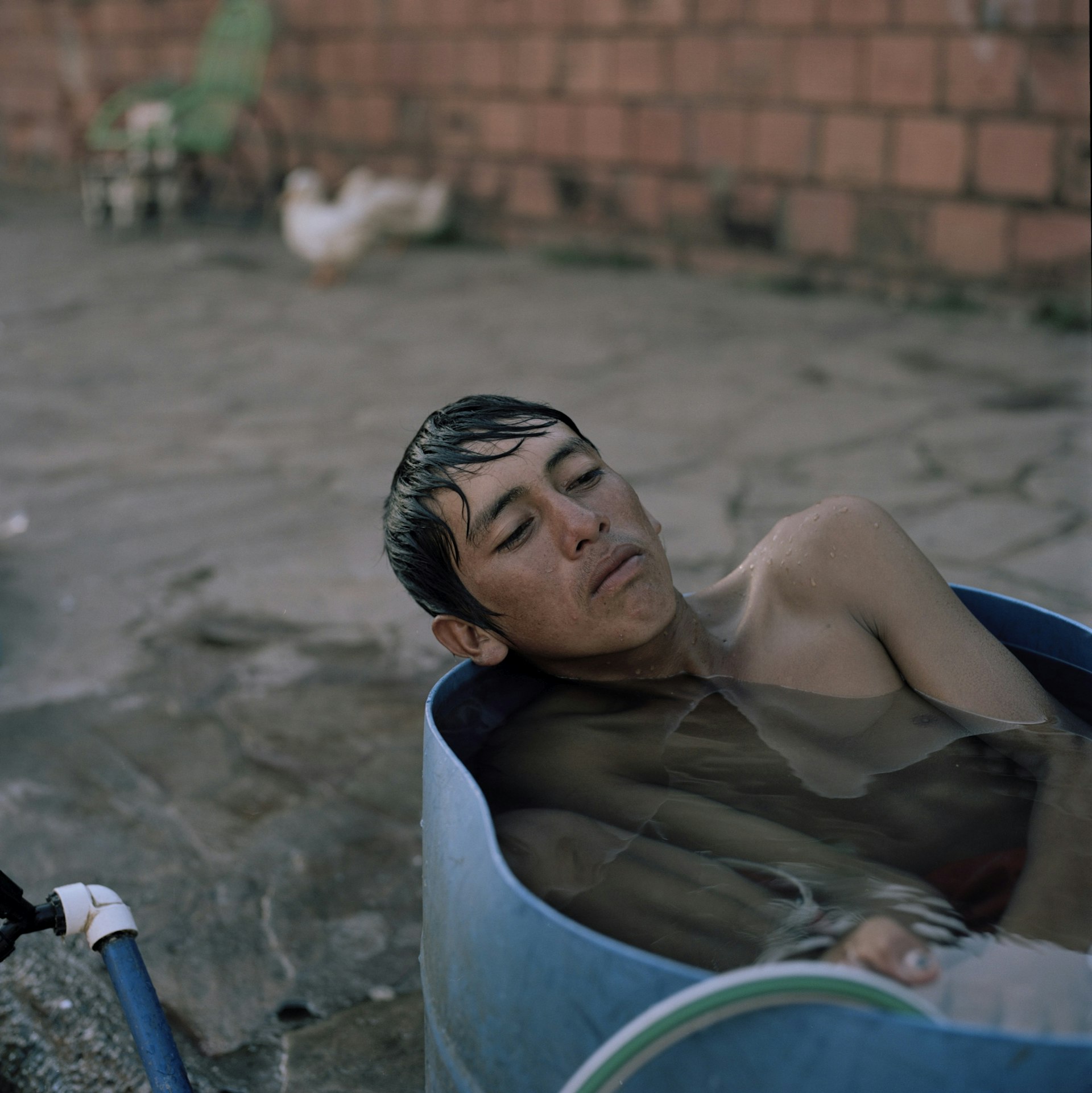 Juan Ramón, 16, takes a bath on a barrel in front of their makeshift home in the streets of Asunción where he has been for eight months together with his family. They were living in the “bañado”, the area surrounding the river until recent floods resulting from El Niño, as well as deforestation due to agribusiness further up the river forced them to evacuate. The bañados have been gradually populated with newcomers on the city, coming from rural areas and with poor perspectives.