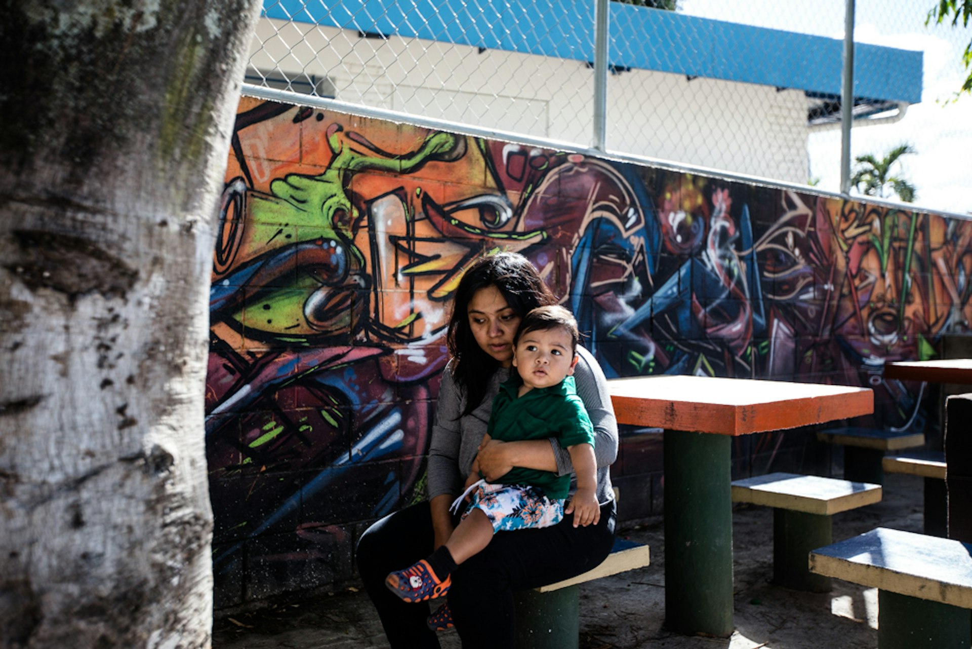 Yerly sits with her son Matías at a local park, next to some graffiti she made for her husband Caesar.