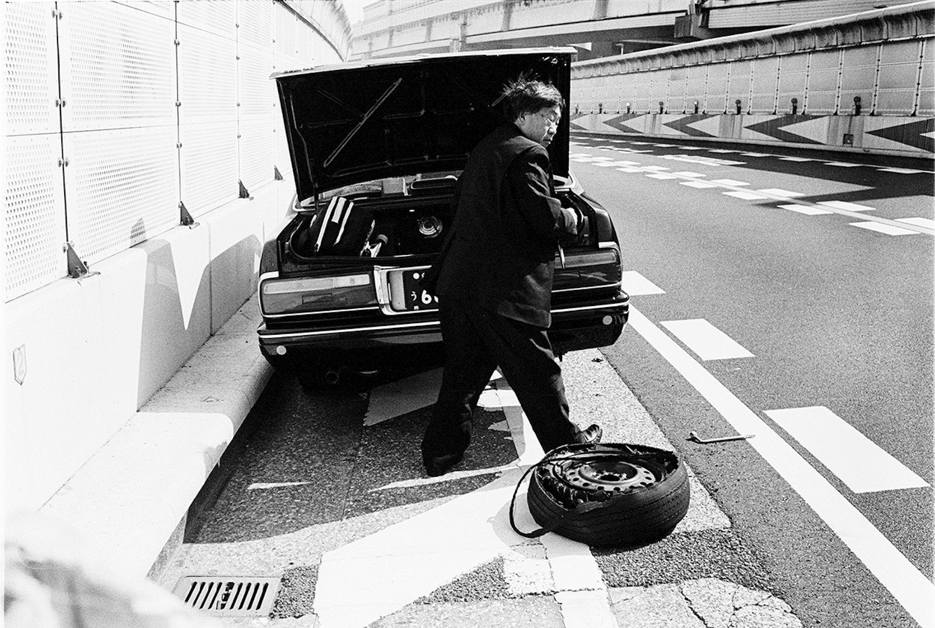 A man in a suit changes the tire of a taxi parked on the side of the road
