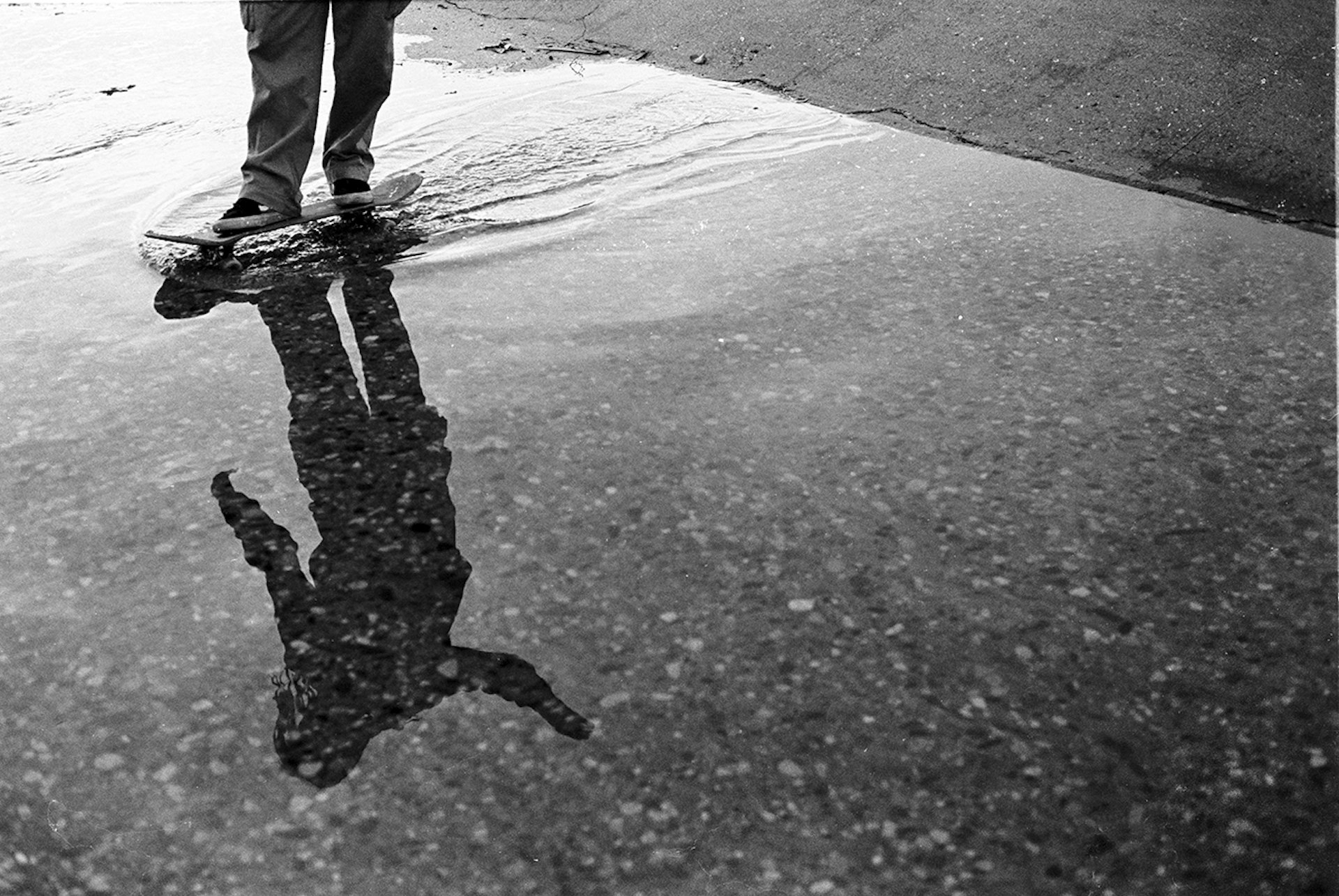 The reflection of a skateboarder in a puddle as they skate through