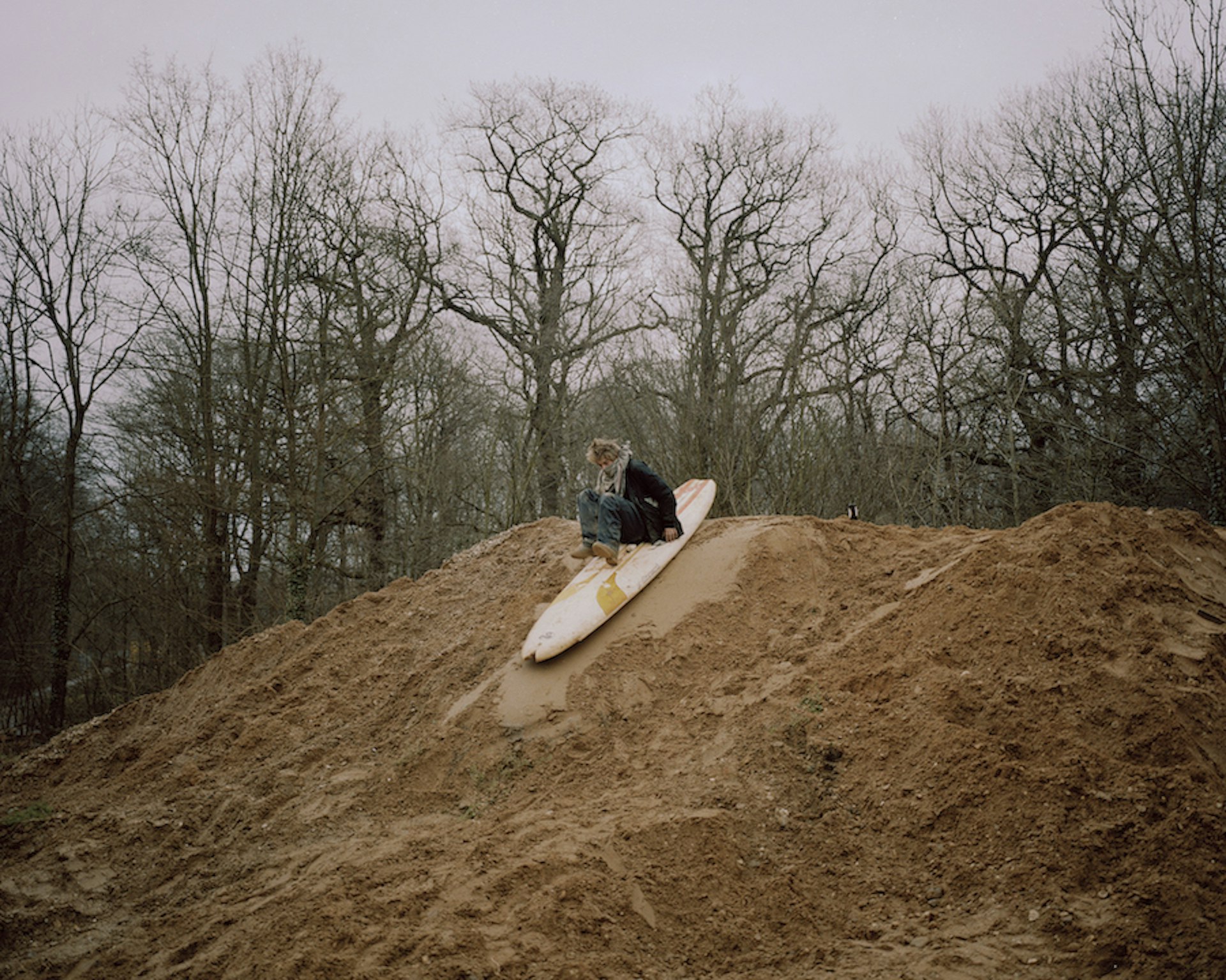 A figure slides down a pile of mud on a surfboard