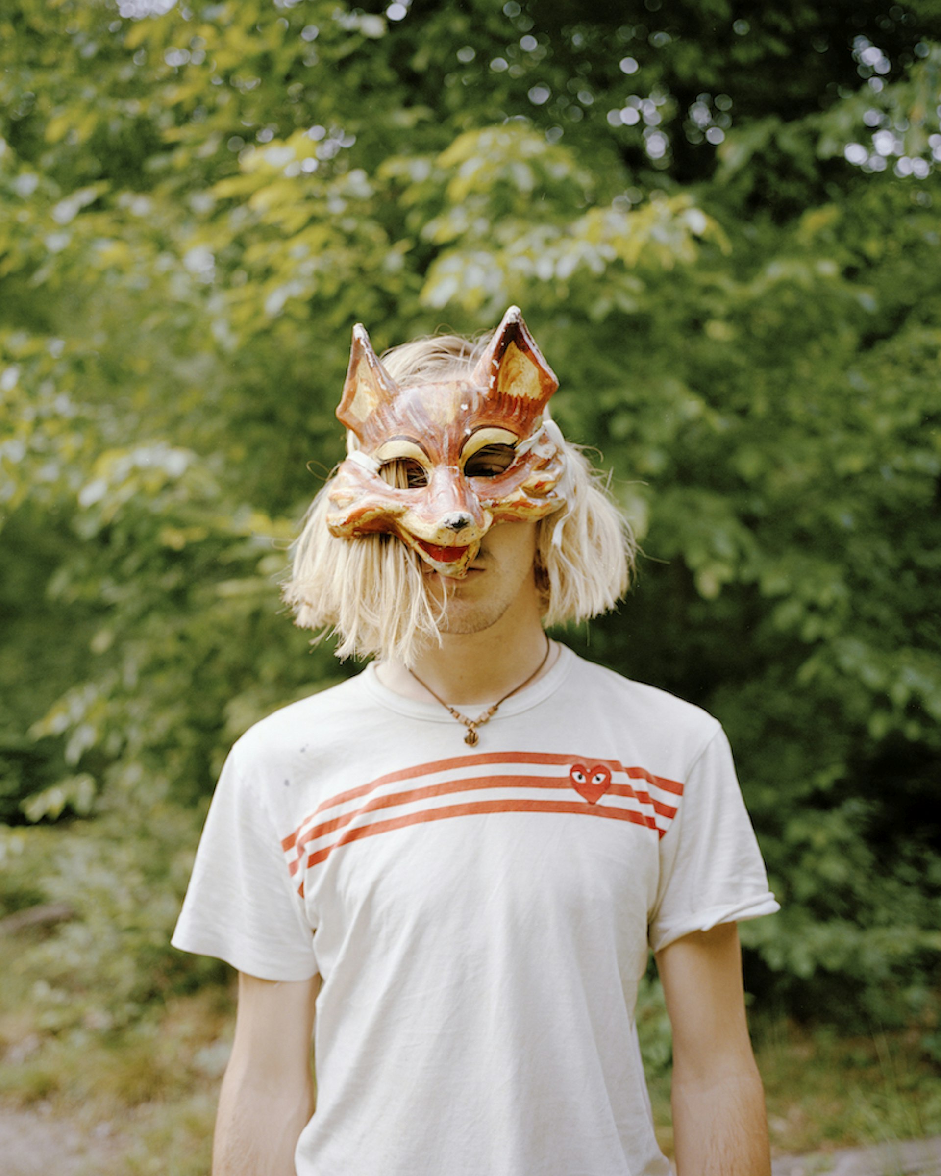 A young man poses for a portrait with a fox mask covering the top of her face